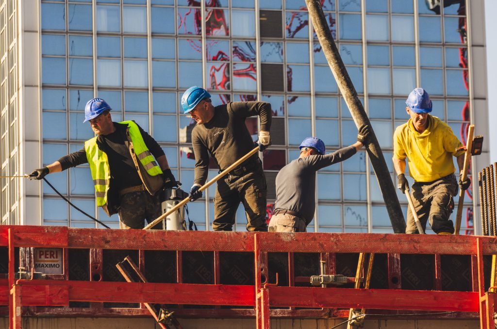 Trabajadores de la construcción en un sitio levantando estructuras con maquinaria, enfocados en el proceso de edificación.